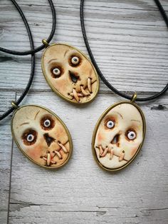 three necklaces with faces and eyes are shown on a white wooden surface, one is wearing