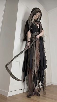 a woman dressed up as a witch holding a large snake in her hand while standing next to a wall