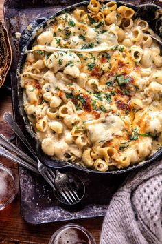 a skillet filled with pasta and sauce on top of a wooden table next to silverware