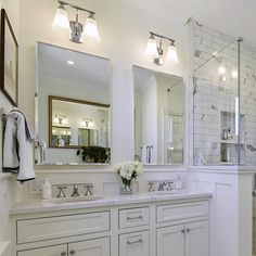 a white bathroom with two sinks, mirrors and lights on the wall next to it