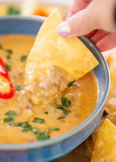 a hand dipping tortilla chips into a bowl of quesadilla soup