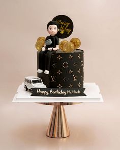 a black and gold birthday cake with a man sitting on the top, surrounded by golden coins