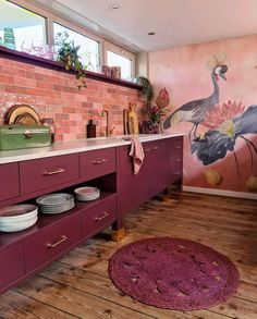 a kitchen with pink walls and wooden floors, painted mural on the wall behind the cabinets