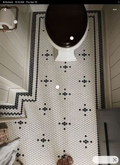 a person standing in front of a black and white bathroom floor with an open toilet