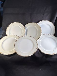 six white and gold plates sitting on top of a black cloth