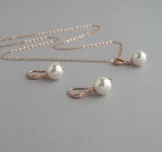 three pieces of jewelry on a gray surface with gold chains and pearls hanging from them