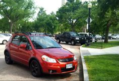 a red car parked on the side of a road next to a park filled with trees