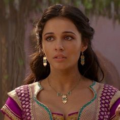 a woman in a purple and gold dress with large earrings on her head looking at the camera