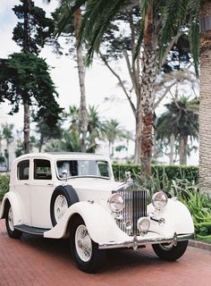 an old fashioned white car parked on the side of a road next to palm trees