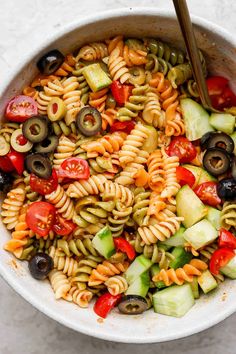 a bowl filled with pasta salad and olives, cucumbers, tomatoes, peppers, and black olives