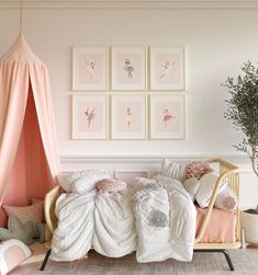 a pink and white bedroom with pictures on the wall, bedding, pillows and rugs