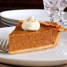 a slice of pumpkin pie on a white plate with a fork and wine glass in the background