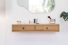 a wooden cabinet with two drawers and a mirror on the wall in a white room