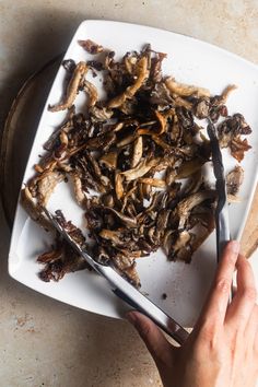 a person is cutting up some food on a white plate with tongs and a wooden spoon