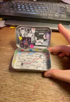 a person is holding an open tin with pictures in it on the table next to a keyboard