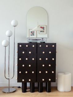 a black cabinet with gold rivets on it and a mirror in the corner