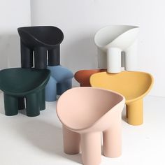 four different colored stools sitting next to each other on a white surface with one chair in the middle