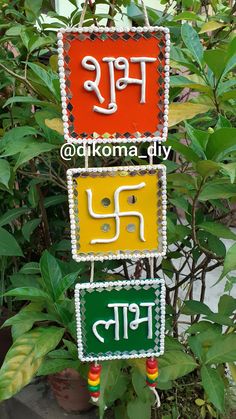 three colorful signs hanging from a tree in front of some bushes and plants with the words om shanti written on them