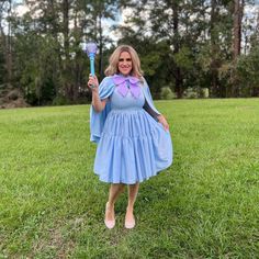 a woman in a blue dress is holding a broom and posing for the camera with trees in the background