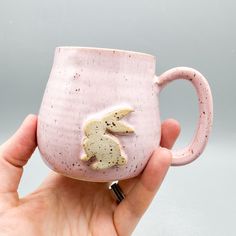 a hand holding a pink coffee mug with two rabbits on it