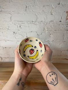 two hands holding a small bowl with designs on it and banana's in the bottom