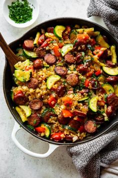 a skillet filled with sausage, zucchini and rice next to a bowl of parsley