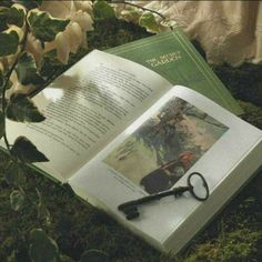 an open book sitting on top of a lush green field next to a pair of scissors