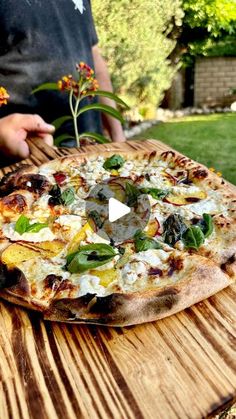 a pizza sitting on top of a wooden table in front of a person holding a plant