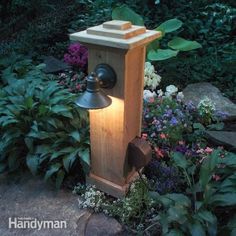 a wooden post with a bell on it in the middle of some plants and flowers