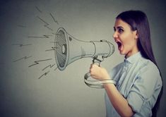 a woman yelling into a megaphone with an arrow drawn on the wall behind her