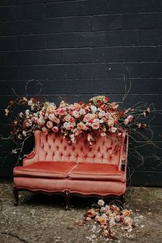 an old pink couch with flowers on it and vines growing out of the back, in front of a brick wall