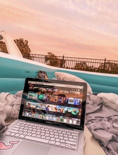 an open laptop computer sitting on top of a bed next to a white surfboard