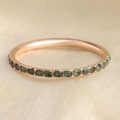 a rose gold band with green sapphires on it's sides, sitting on a white cloth