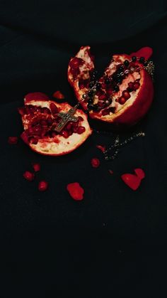 two pomegranates cut in half on a black surface with petals scattered around them