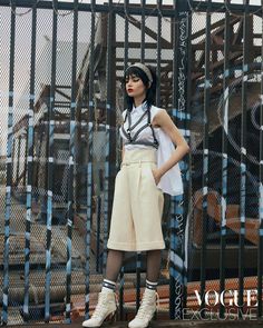 a woman standing in front of a fence with her hands on her hips and looking at the camera