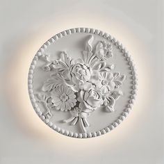 a white circular light fixture with flowers on the front and sides, mounted on a wall