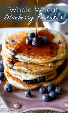 blueberry pancakes with syrup being drizzled over them on a pink plate