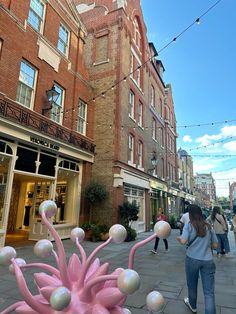 a woman walking down a street next to tall buildings with balloons floating in the air