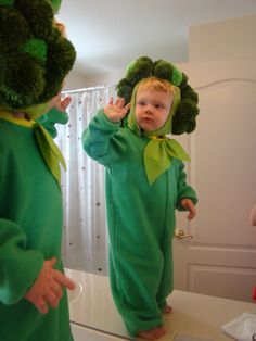 a young child in a green costume is looking at herself in the mirror and waving