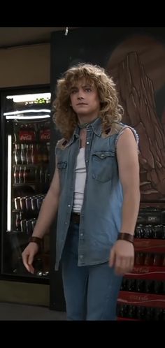 a woman with curly hair standing in front of a vending machine and looking at the camera