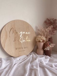 a wooden sign sitting on top of a white bed next to vases and flowers