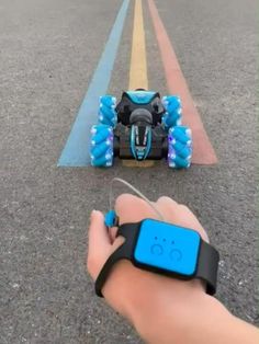 a hand is holding a remote control car on the road with blue wheels and tires