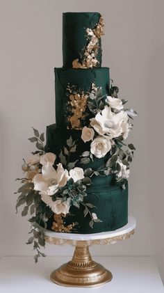 a green and gold wedding cake with white flowers on the top tier is sitting on a table