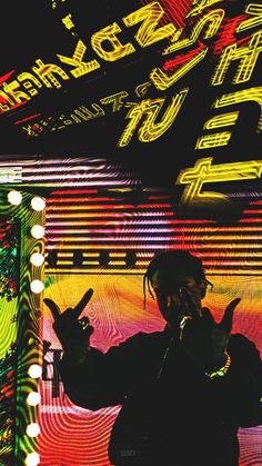 a man with dreadlocks standing in front of a neon sign and giving the peace sign