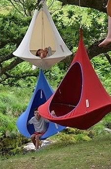 three people hanging upside down hammocks in the woods