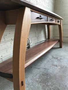 a wooden table with two drawers and a shelf underneath it on concrete floor next to brick wall