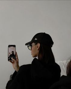 a woman taking a selfie with her cell phone while wearing a hat and glasses