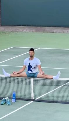 a man sitting on top of a tennis court holding a racquet next to a net