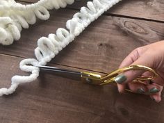 a person is holding scissors over yarn on a wooden table with white and gold letters