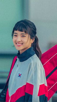 a woman holding a red surfboard in her right hand and smiling at the camera